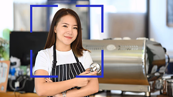 Barista preparing espresso in a café setting, holding a portafilter beside a commercial machine.